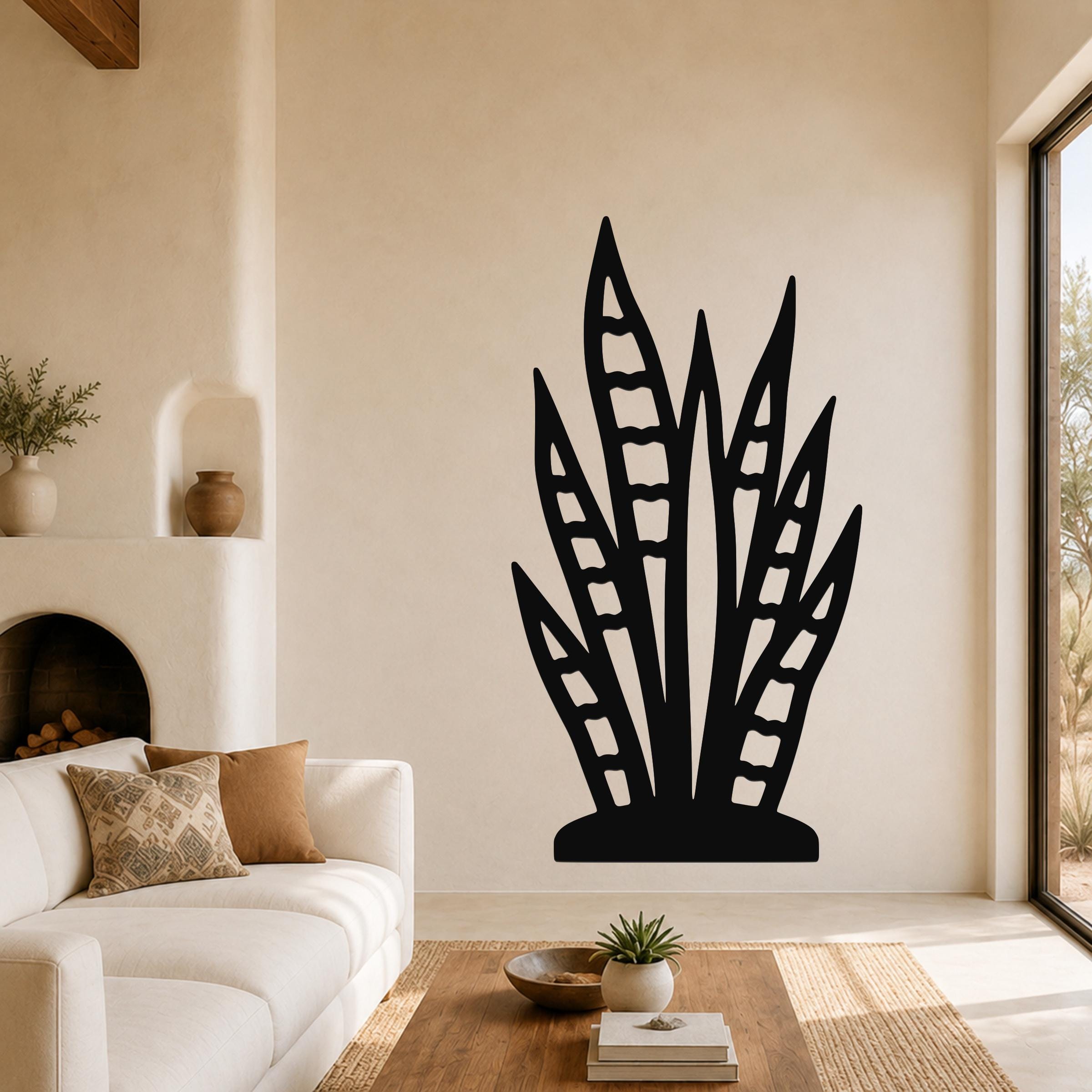 Black metal wall art in the shape of a snake plant with leaf cutouts, mounted on a living room wall above a white sofa.