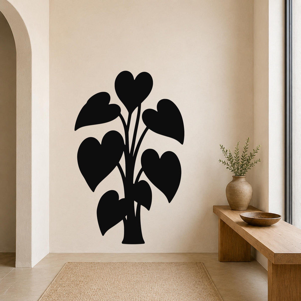 Black metal wall art in the silhouette of a heart-leaf philodendron plant, mounted on a beige living room wall above a woven rug.