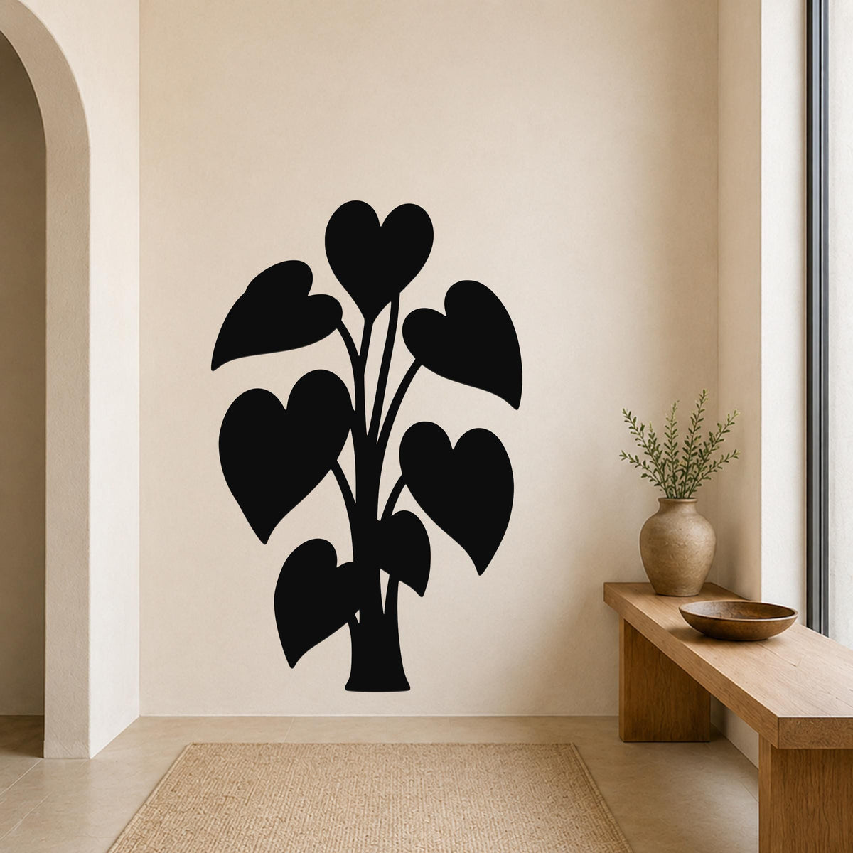 Black metal wall art in the silhouette of a heart-leaf philodendron plant, mounted on a beige living room wall above a woven rug.