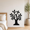 Black metal wall art in the shape of a tree with leafy branches, mounted on a white wall above a bed in a bedroom.