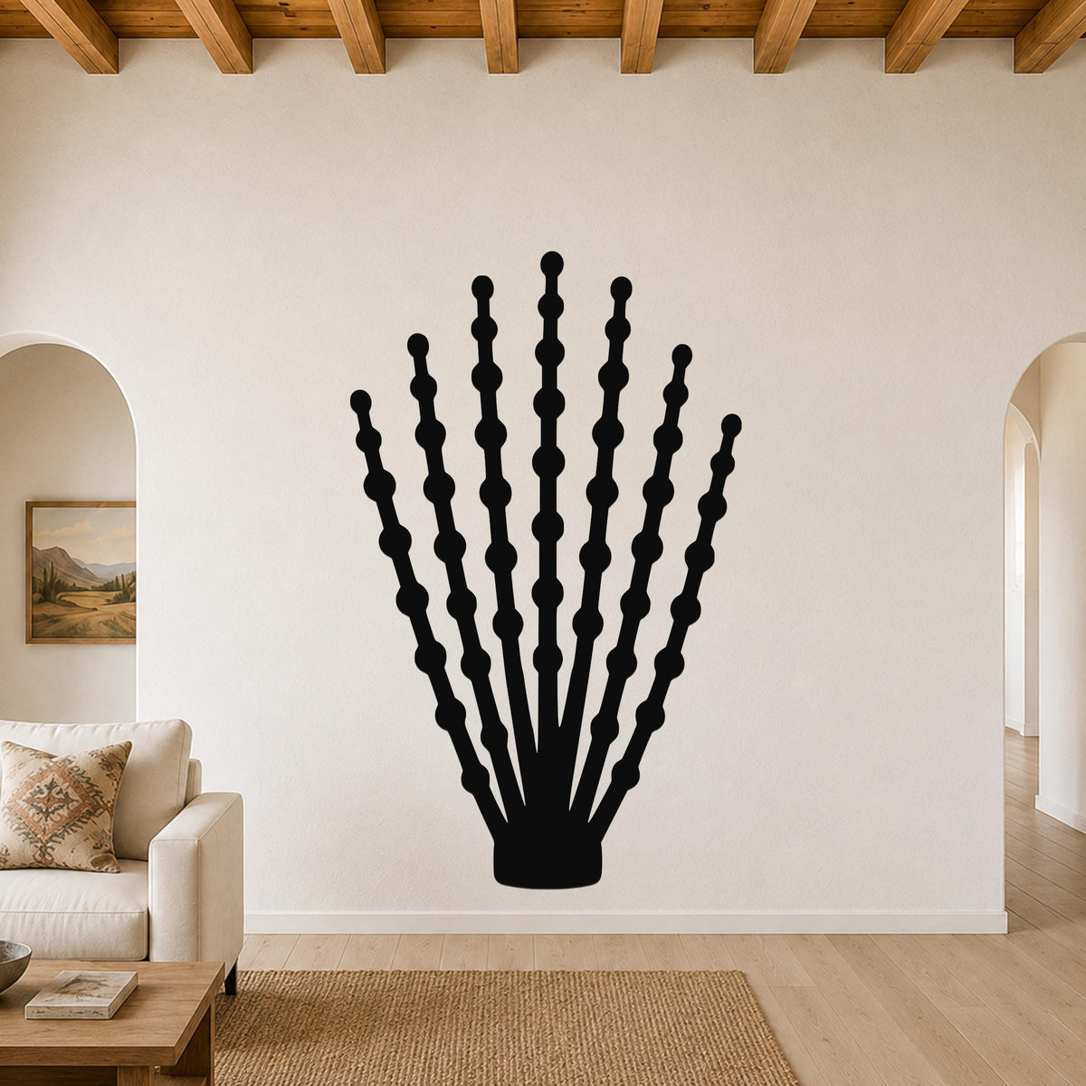 Black metal ocotillo wall art with branching stem and bead-like cutouts, mounted on a living room wall above a sofa.