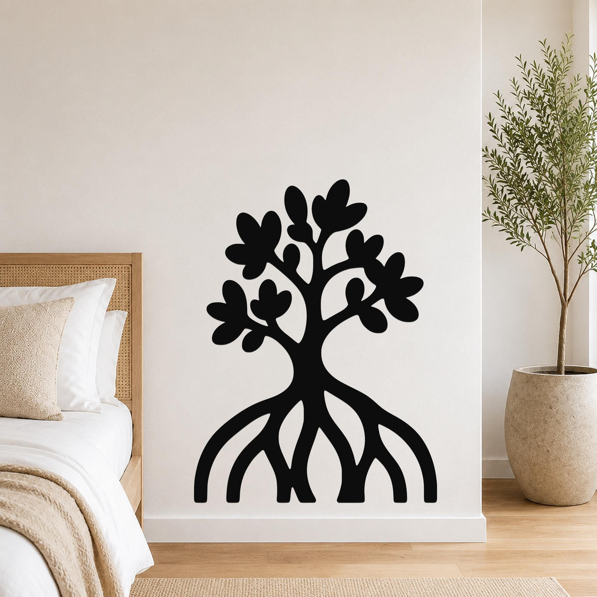 Black metal wall art in a tree silhouette with visible root and leaf cutouts, mounted on a white wall above a bed in a bedroom.