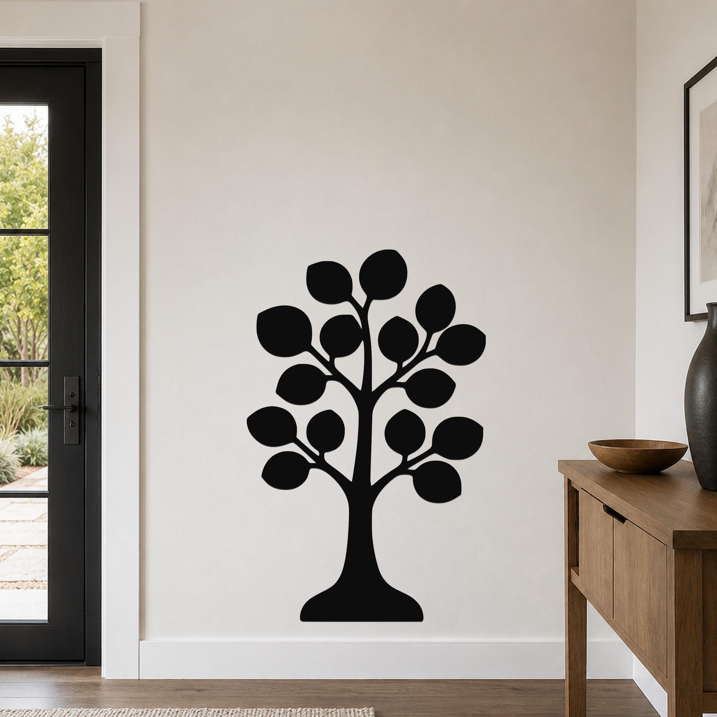 Black metal wall art in the shape of a stylized tree with circular leaf cutouts, mounted on a light-colored wall above a wooden console table in a modern entryway.