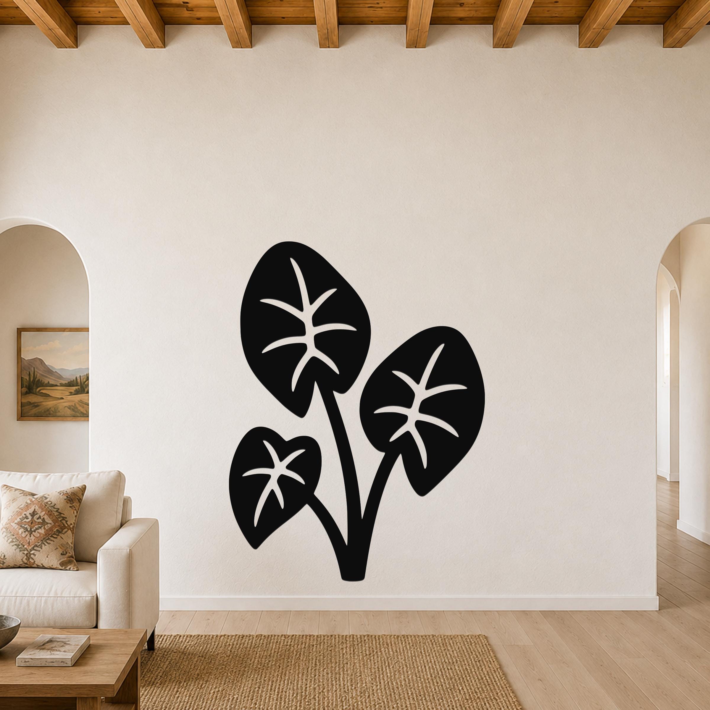 Black metal wall art featuring a silhouette of three elephant ear leaves with internal vein cutouts, mounted on a living room wall above a sofa.