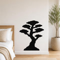 Black metal bonsai tree wall art with layered canopy cutouts, mounted on a white bedroom wall above a bed.