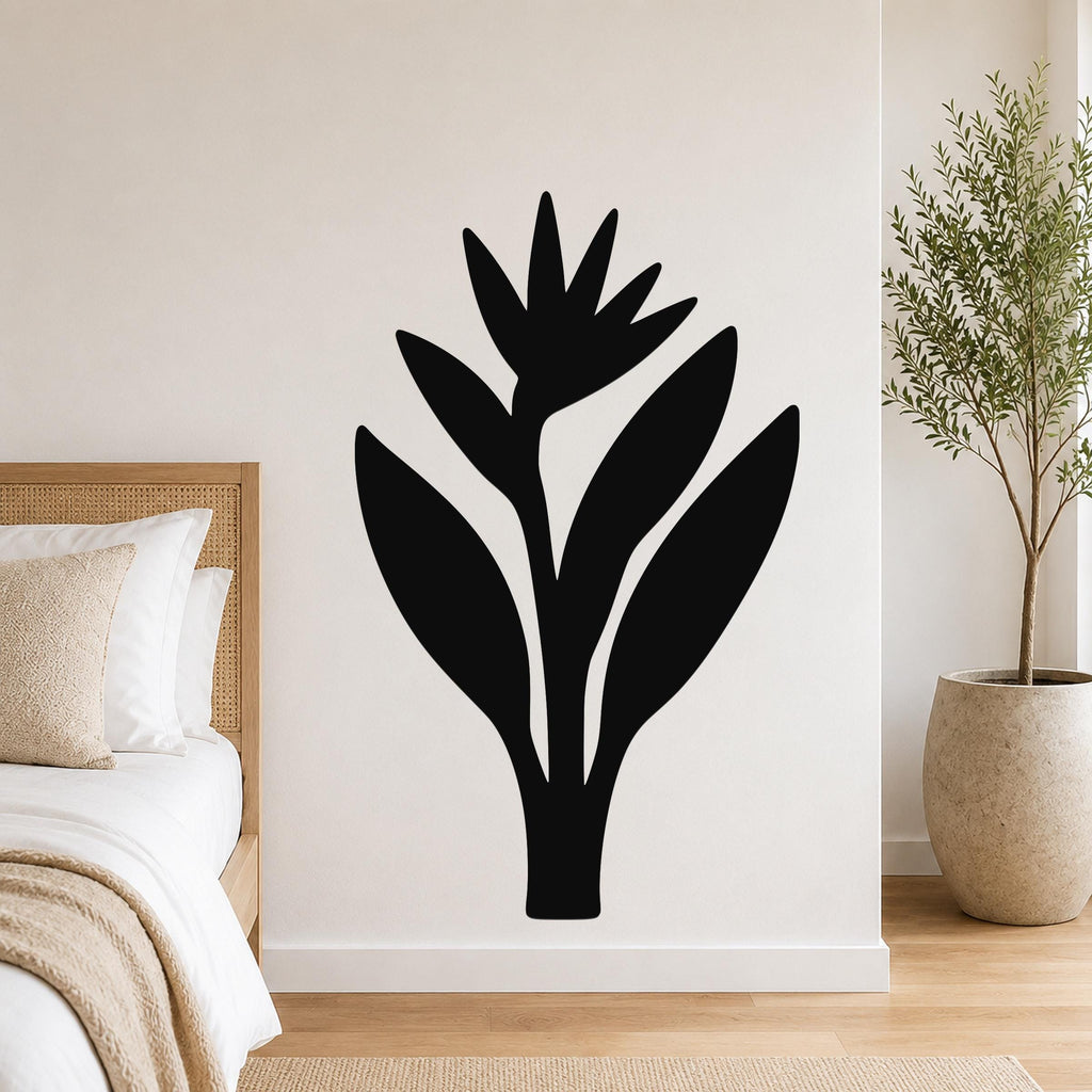 Black metal wall art in the silhouette of a bird of paradise plant, mounted on a white bedroom wall above a bed with a woven headboard.