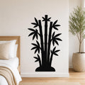 Black metal wall art silhouette of a bamboo cluster with multiple stalks and leaves, mounted on a white wall above a bed in a bedroom.