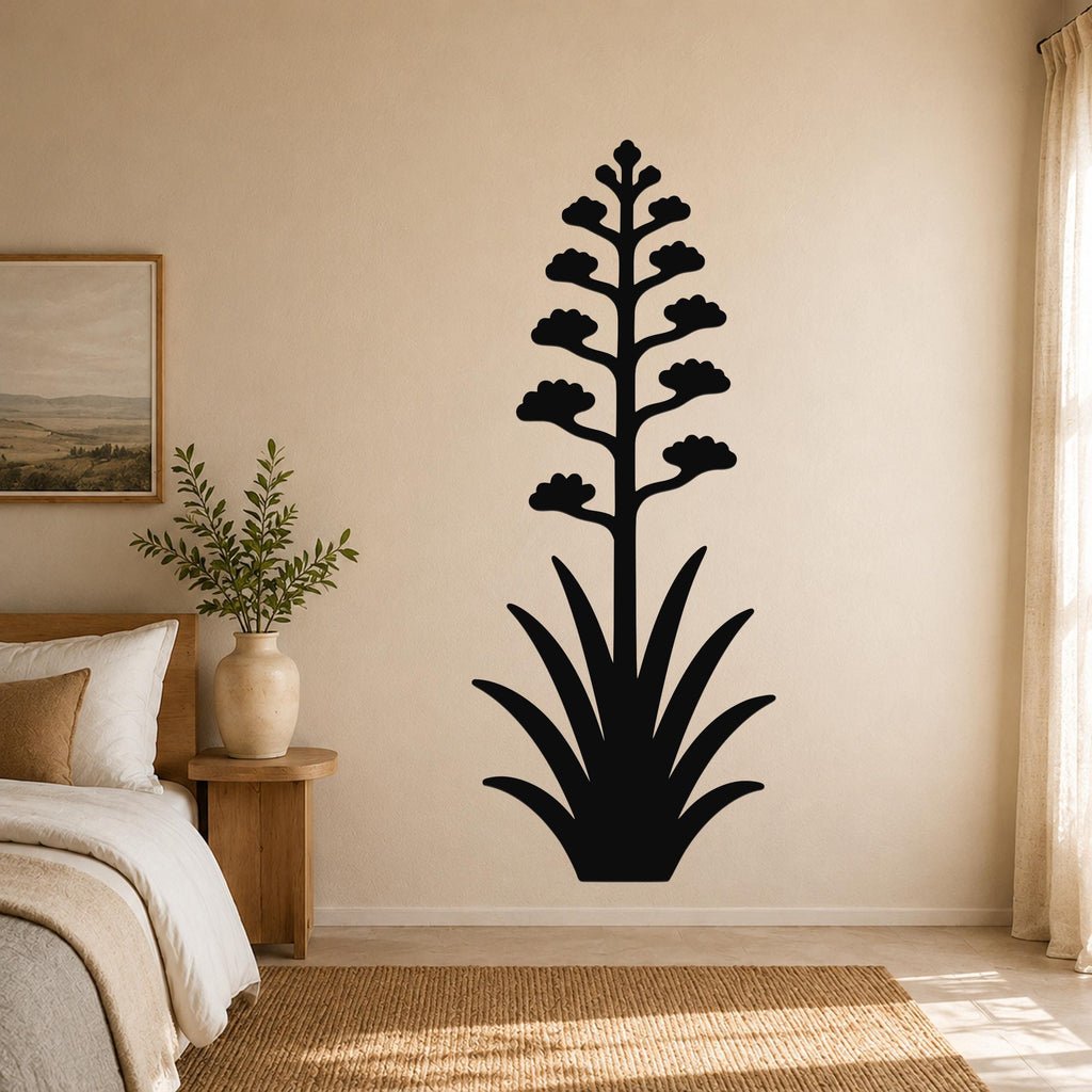Black metal wall art in the silhouette of a blooming agave plant with a tall flower stalk and spiky leaves, mounted on a beige wall above a bed in a bedroom.