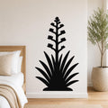 Black metal wall art silhouette of a blooming agave plant with spiky leaves and flower stalk, mounted on a bedroom wall above a bed.