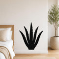 Black metal agave wall art with spiky leaf cutouts, mounted on a white bedroom wall above a bed.