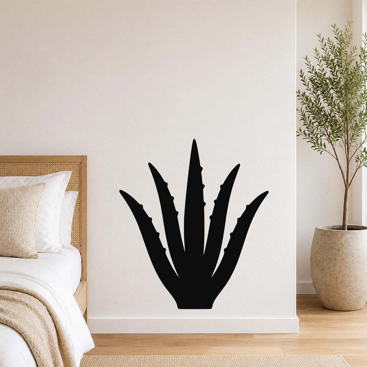 Black metal agave wall art with spiky leaf cutouts, mounted on a white bedroom wall above a bed.