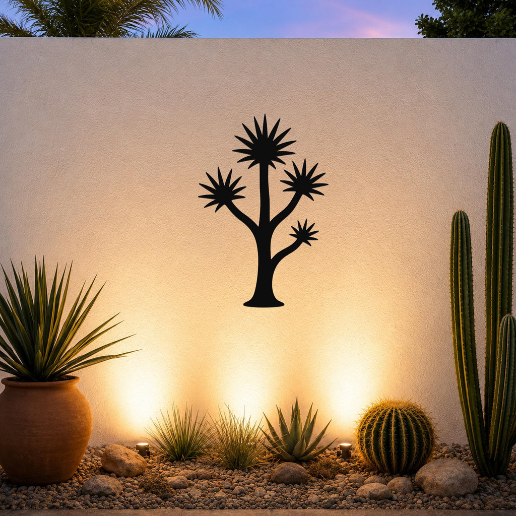 Black metal wall art in a tall yucca silhouette with starburst leaves, mounted on an outdoor wall above a desert garden with cacti and warm uplighting.