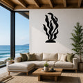 Black metal kelp wall art with flowing leaf cutouts, mounted on a white living room wall above a beige sectional sofa.