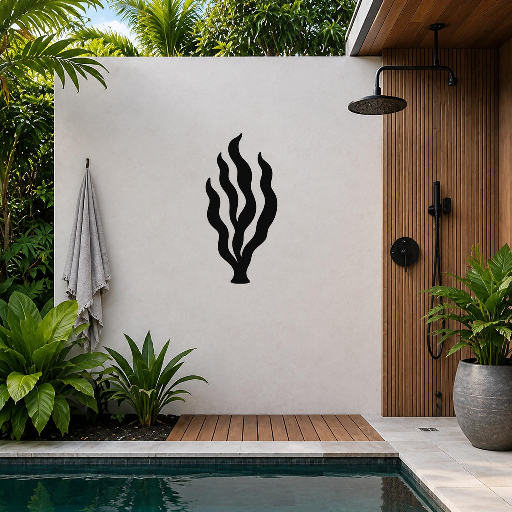Black metal kelp seaweed wall art with flowing frond cutouts, mounted on a white outdoor wall beside a pool and shower area.