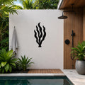 Black metal kelp seaweed wall art with flowing frond cutouts, mounted on a white outdoor wall beside a pool and shower area.