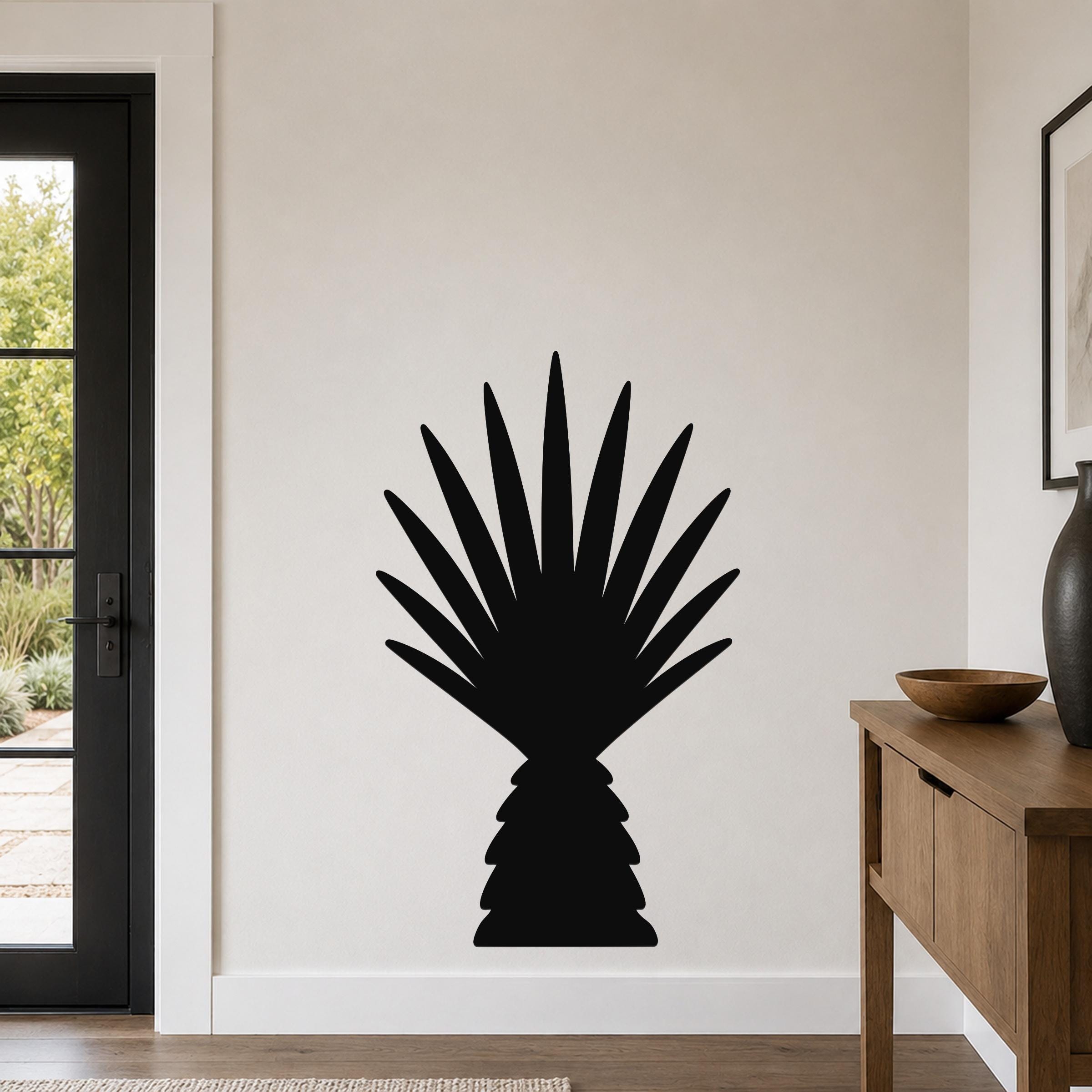 Black metal wall art in the silhouette of a baby California fan palm tree, mounted on a light-colored wall in a modern entryway.