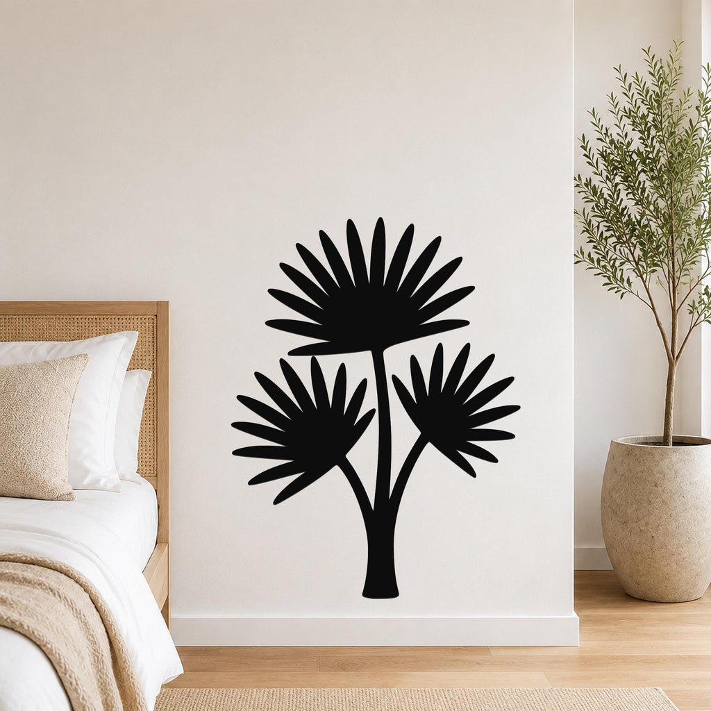 Black metal wall art cutout of a fan palm tree with three fronds, mounted on a white wall above a bed in a bedroom.