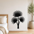 Black metal wall art cutout of a fan palm tree with three fronds, mounted on a white wall above a bed in a bedroom.