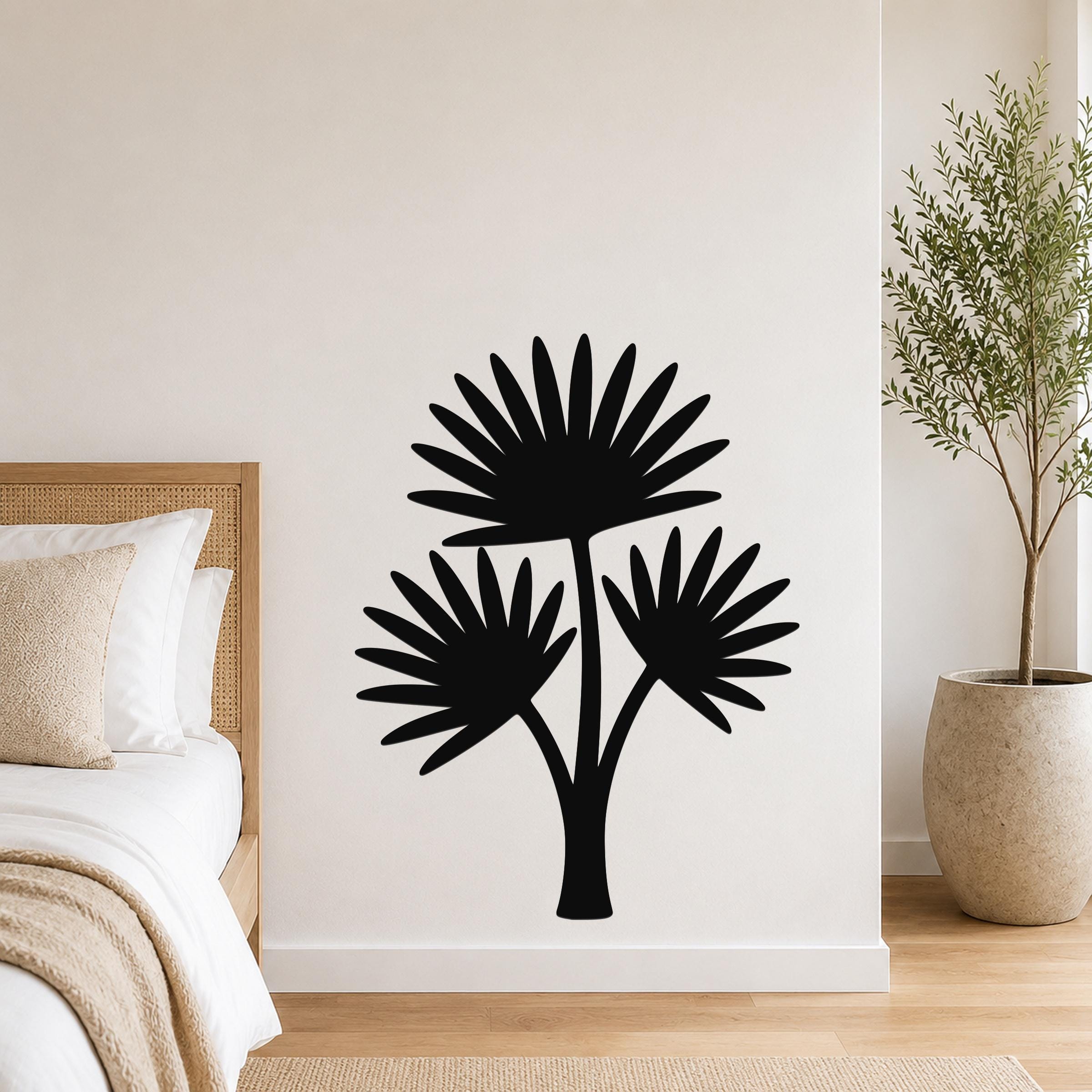 Black metal wall art cutout of a fan palm tree with three fronds, mounted on a white wall above a bed in a bedroom.