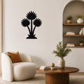 Black metal wall art featuring a silhouette of three wildflowers, mounted on a living room wall above a round wooden coffee table.