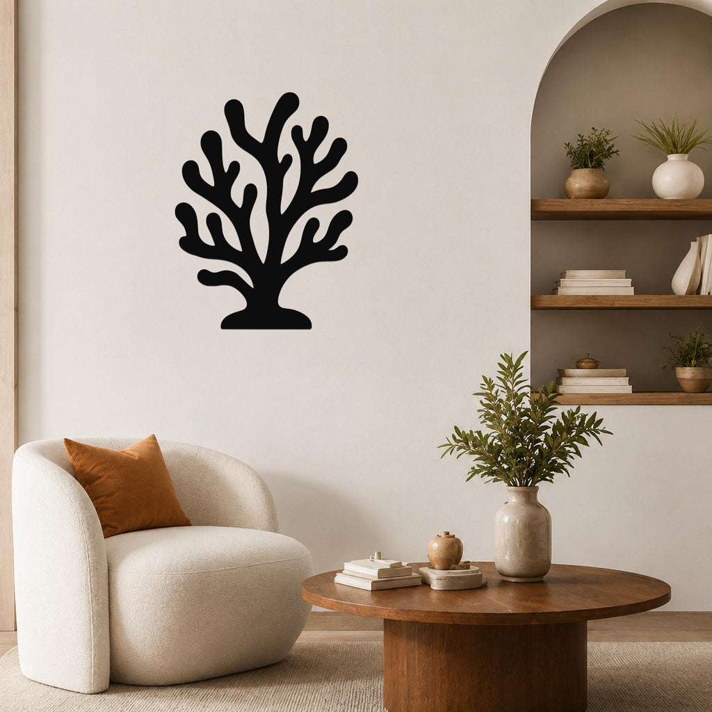 Black metal coral wall art with branching cutouts, mounted on a living room wall above a white armchair.