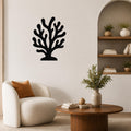 Black metal coral wall art with branching cutouts, mounted on a living room wall above a white armchair.