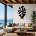 Black metal coral wall art with branching cutouts, mounted on a white wall above a beige sectional sofa in a living room with ocean views.