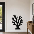 Black metal coral wall art with branching cutouts, mounted on a living room wall above a wooden console table.