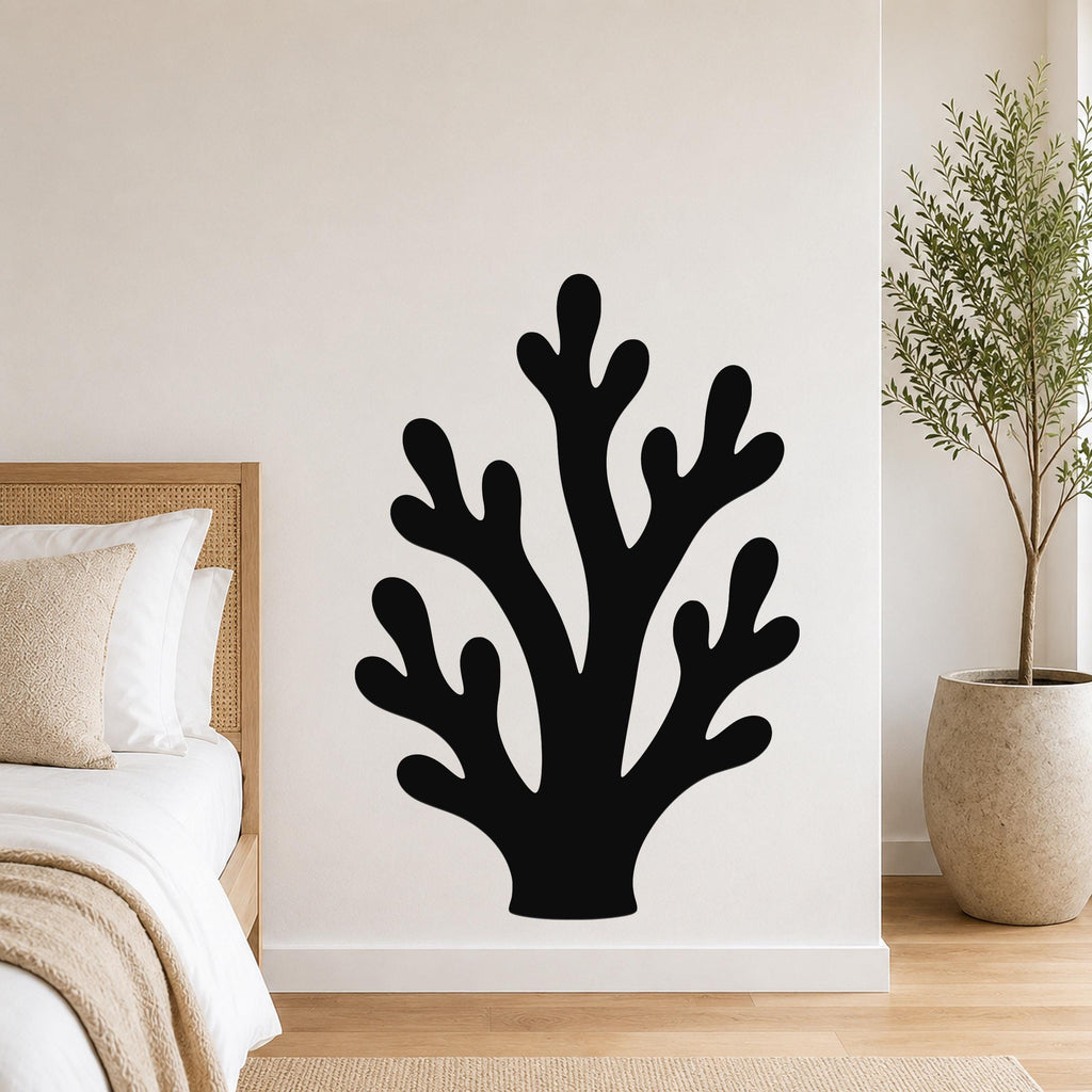 Black metal wall art in a branching coral silhouette, mounted on a white bedroom wall above a bed with a woven headboard.