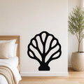 Black metal wall art in a fan coral silhouette with internal cutouts, mounted on a white bedroom wall above a bed.