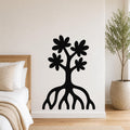 Black metal wall art in a tree silhouette with flower cutouts and exposed roots, mounted on a bedroom wall above a bed.