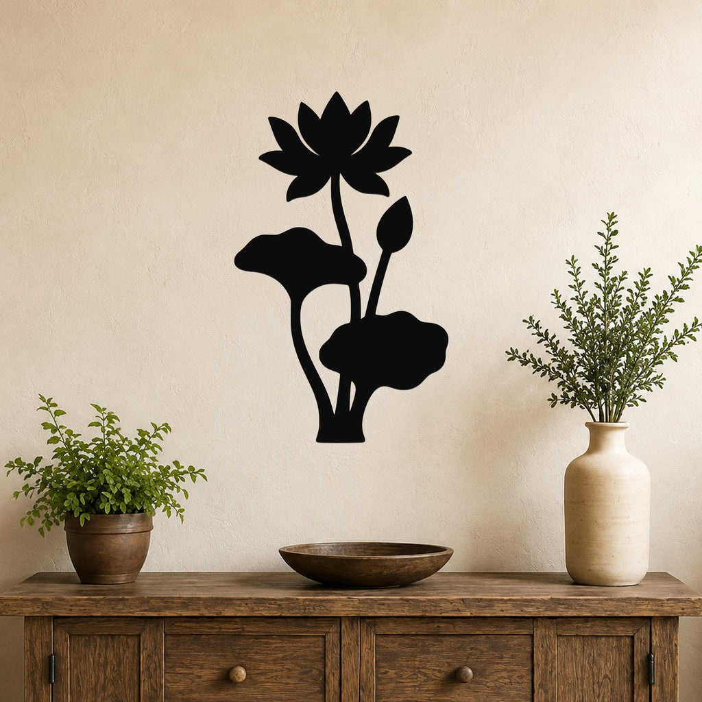 Black metal lotus wall art with a flower, bud, and leaves in a silhouette style, mounted on a beige wall above a wooden console table with plants.