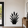 Black metal cattail wall art silhouette with three seed heads and long leaves, mounted on a white wall in a living room near a door and wooden console table.