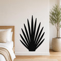 Black metal wall art in a fan-shaped agave silhouette, mounted on a white bedroom wall above a bed with a woven headboard.