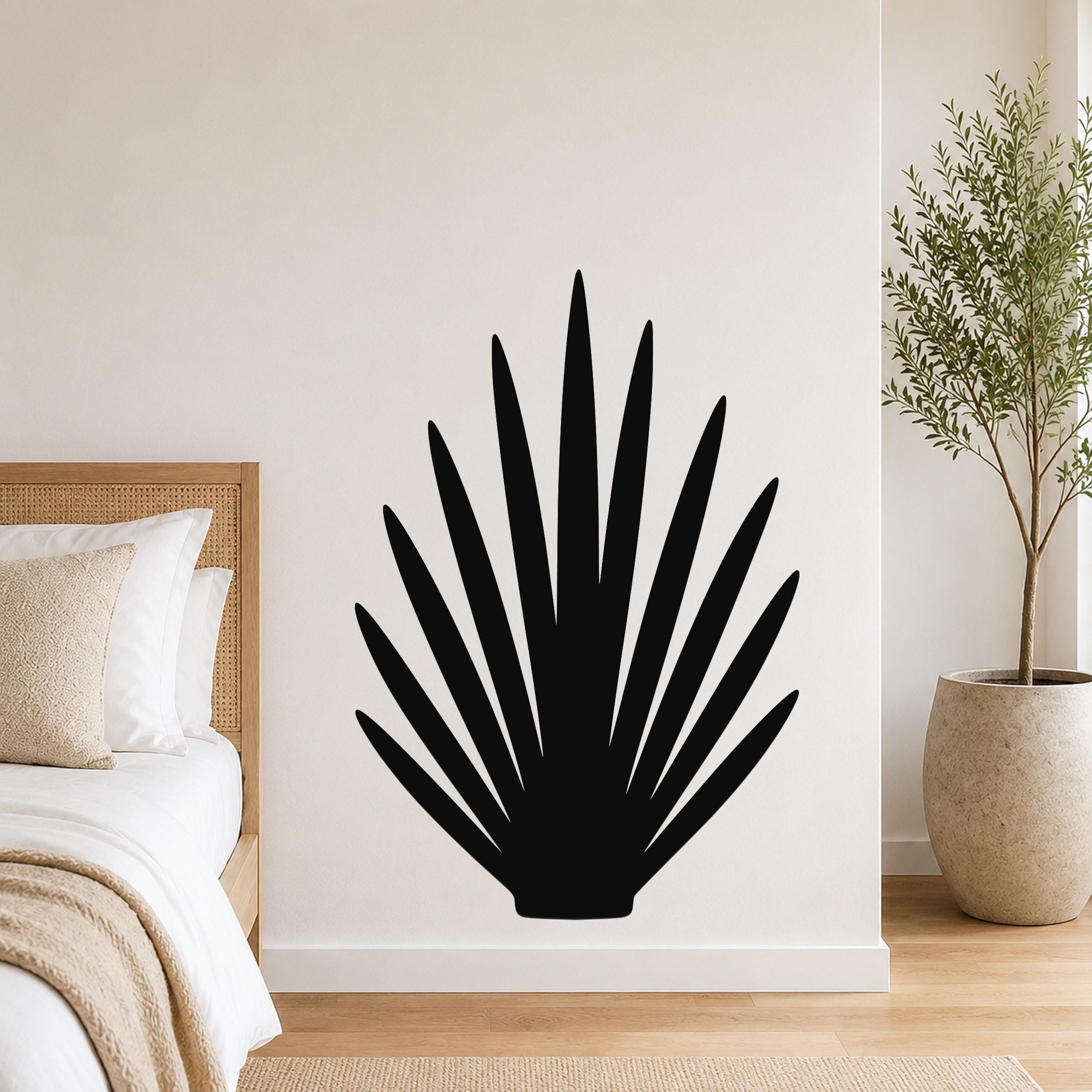 Black metal wall art in a fan-shaped agave silhouette, mounted on a white bedroom wall above a bed with a woven headboard.