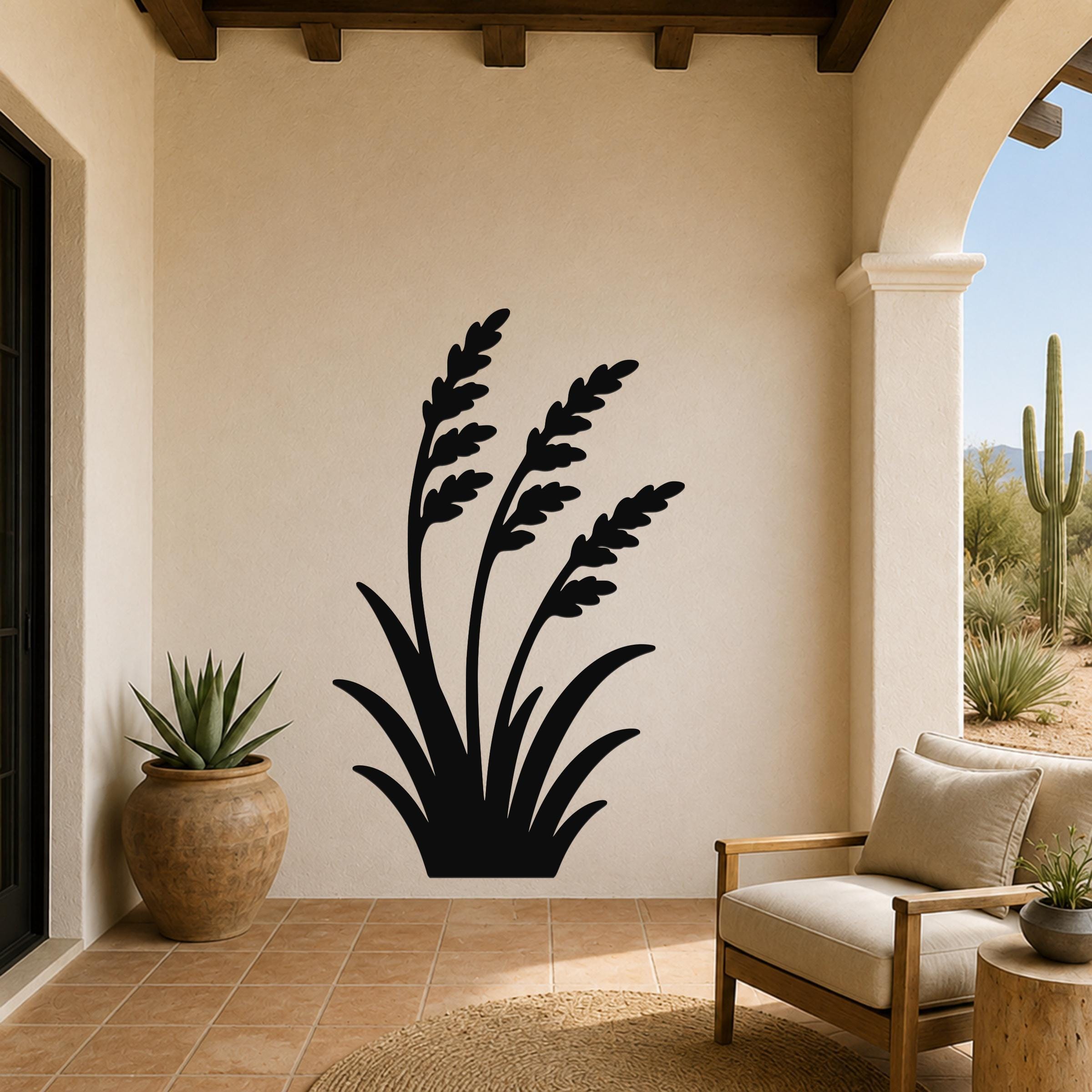 Black metal wall art in a wild grass silhouette design, mounted on a beige stucco wall above a patio seating area.