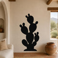 Black metal prickly pear cactus wall art with multiple pads and cutout details, mounted on a beige living room wall above a sofa.