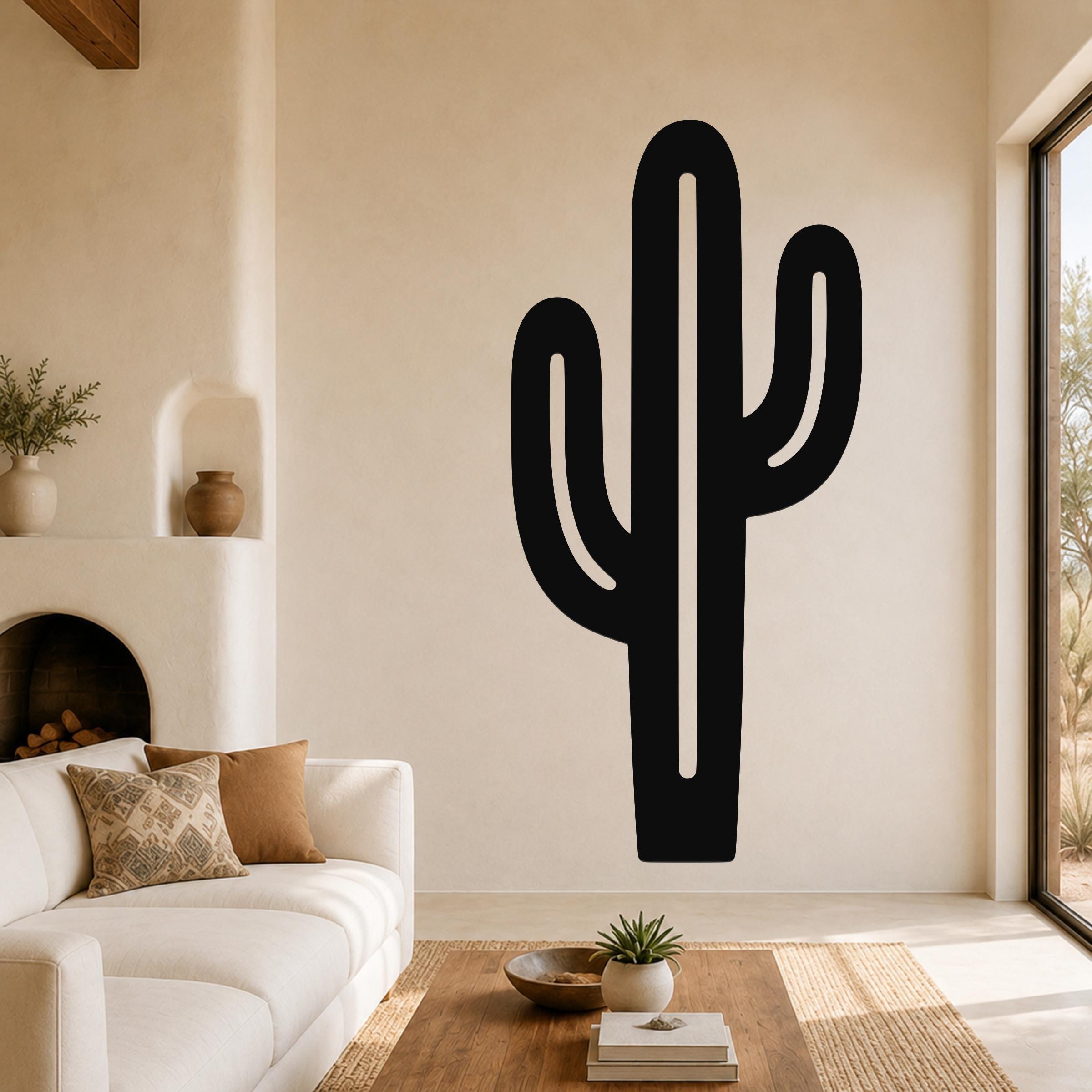 Black metal saguaro cactus wall art with cutout arms, mounted on a living room wall above a white sofa.