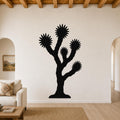 Black metal Joshua tree wall art with starburst-shaped branches, mounted on a living room wall above a sofa.
