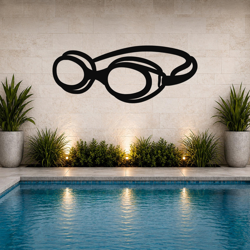 Black metal swim goggles wall art with a bold silhouette design, mounted on a tiled wall above a poolside garden with potted plants and ambient lighting.