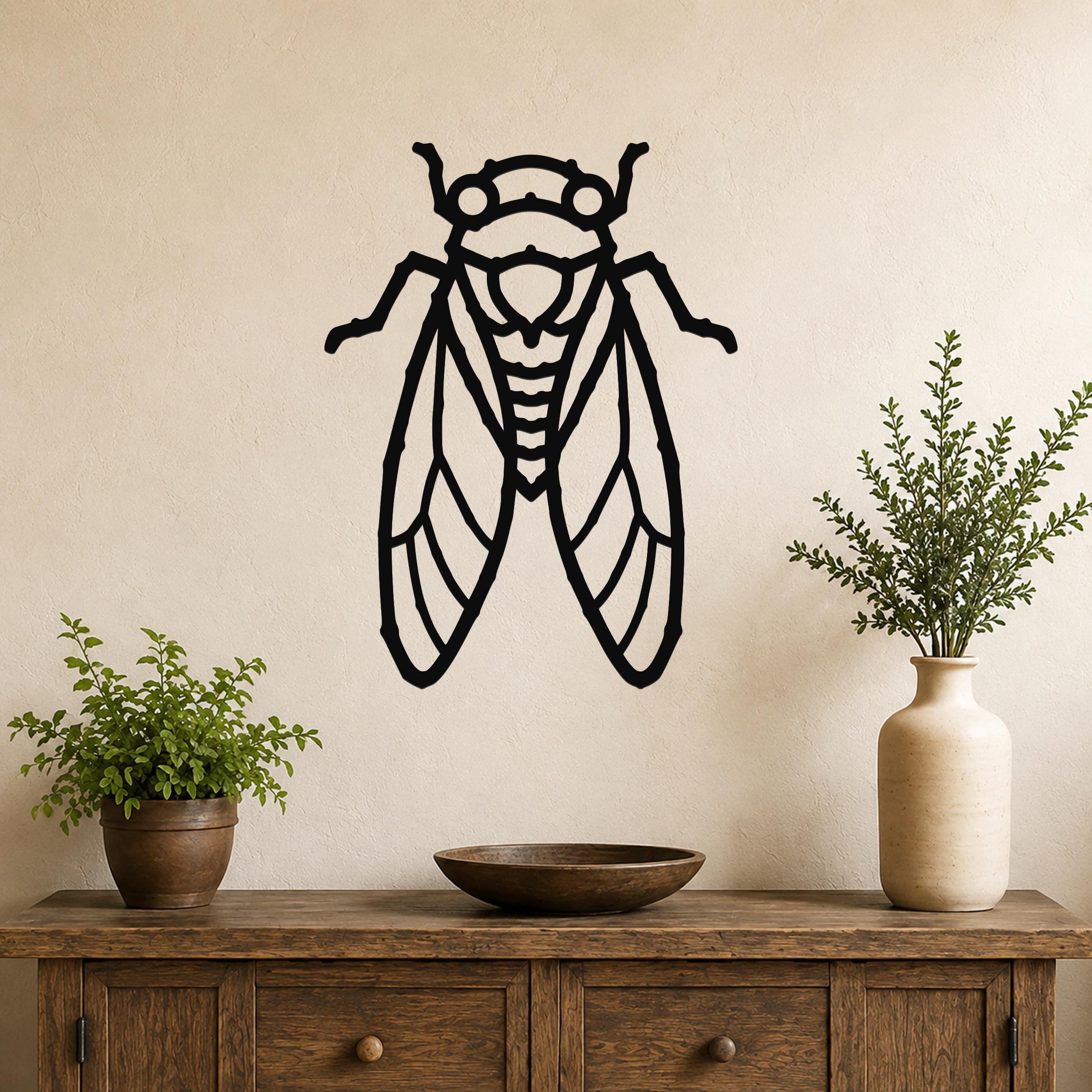 Black metal cicada wall art with detailed wing and body cutouts, mounted on a beige wall above a wooden console table with potted plants.