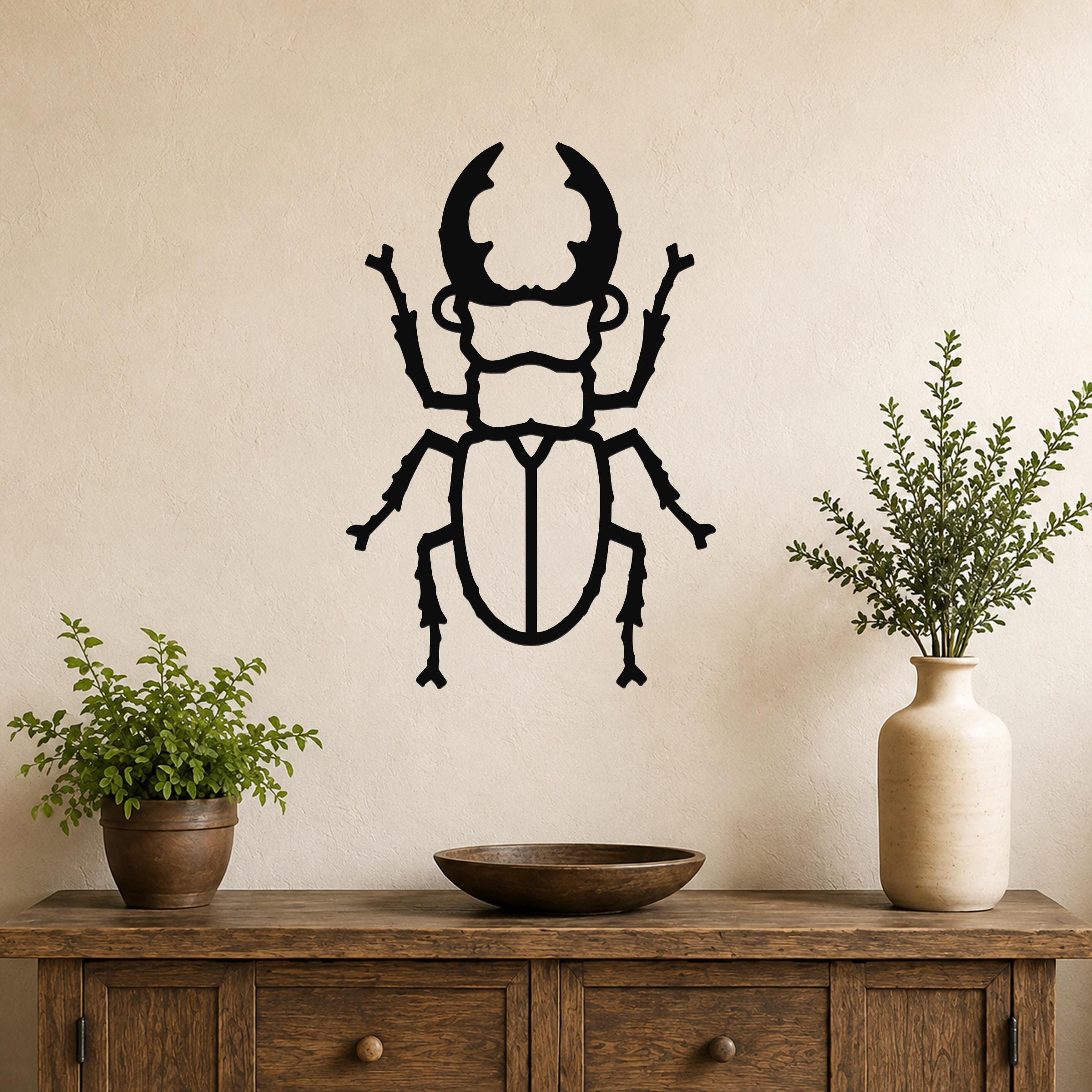 Black metal beetle wall art with detailed cutout silhouette, mounted on a beige wall above a wooden console table with potted plants.