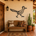 Black metal roadrunner wall art with motion-line cutouts, mounted on a stucco wall above a wooden bench in a patio entryway.