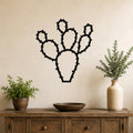 Black metal wall art in the silhouette of a prickly pear cactus with segmented pads and spines, mounted on a beige wall above a wooden console table.