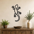 Black metal gecko wall art with a cutout silhouette design, mounted on a beige wall above a wooden console table in a living room.