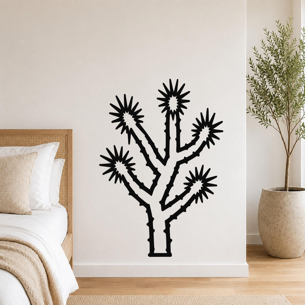 Black metal Joshua tree wall art with starburst cutouts, mounted on a white bedroom wall above a bed.