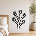 Black metal Joshua tree wall art with starburst cutouts, mounted on a white bedroom wall above a bed.