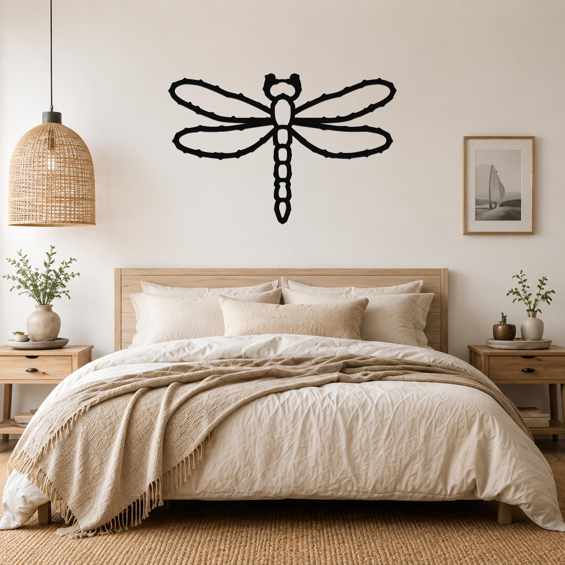 Black metal dragonfly wall art with detailed wing and body cutouts, mounted above a wooden bed in a neutral bedroom.