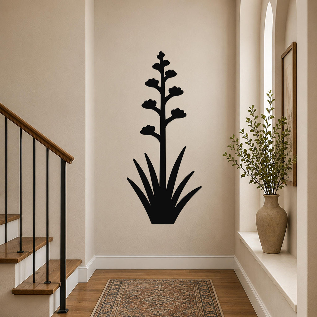Black metal agave wall art with a tall flowering stalk and spiky leaves, mounted on a hallway wall above a patterned rug near a staircase.