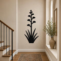 Black metal agave wall art with a tall flowering stalk and spiky leaves, mounted on a hallway wall above a patterned rug near a staircase.